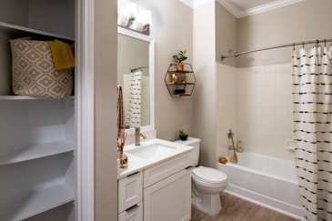 A contemporary bathroom at The Pointe at Vista Ridge featuring shelving, a vanity, and a bathtub, designed for convenience and comfort.