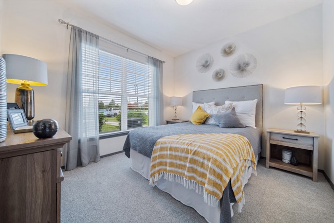 Comfortable and relaxing furnished grey and white apartment bedroom with a large window and yellow throw on the bed
